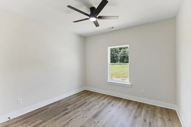 an empty room with wooden floor ceiling fan and windows