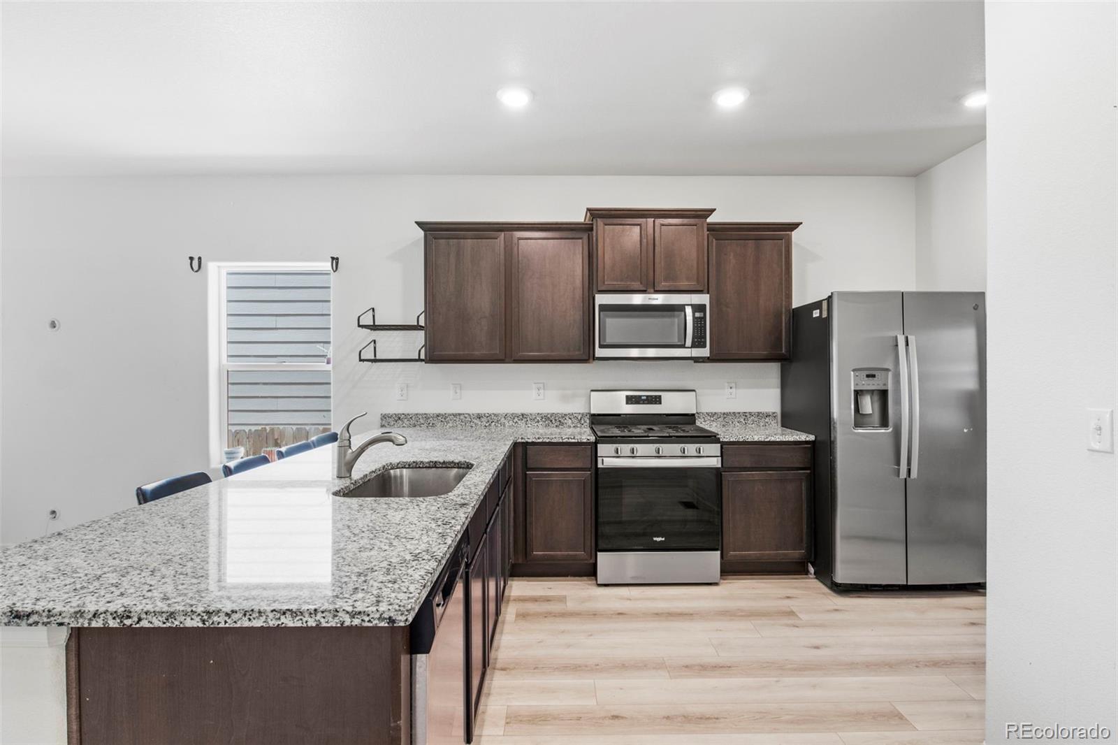 311 Maple Street Bennett, CO 80102 - Photo 13 of 35 a kitchen with granite countertop kitchen island stainless steel appliances a sink stove refrigerator and cabinets