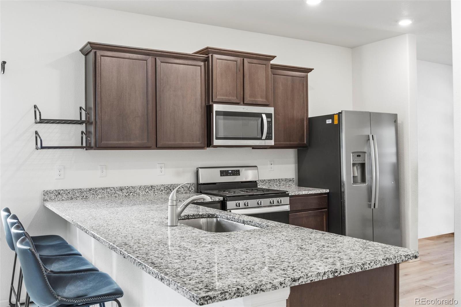 311 Maple Street Bennett, CO 80102 - Photo 14 of 35 a kitchen with granite countertop a sink a stove a refrigerator and a cabinets
