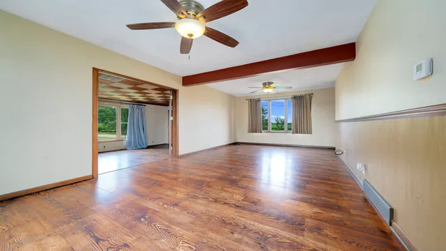an empty room with wooden floor chandelier fan and windows