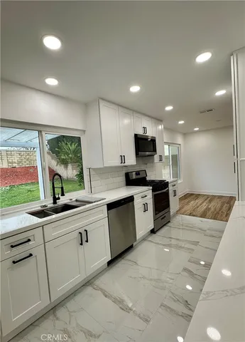 a large kitchen with granite countertop a large counter top stainless steel appliances and white cabinets