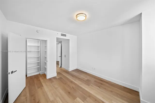 a view of an empty room with wooden floor and closet