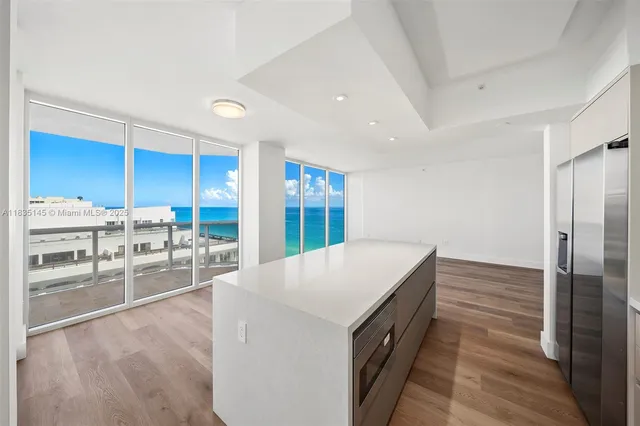 a living room with stainless steel appliances kitchen island granite countertop a refrigerator a oven a sink with wooden cabinets and floor