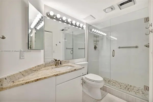 a bathroom with a granite countertop sink a toilet a mirror and shower