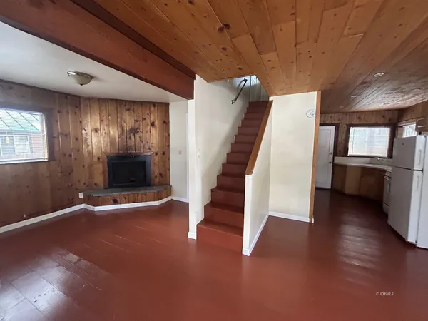 an empty room with wooden floor staircase and windows