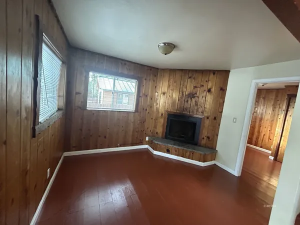 an empty room with wooden floor fireplace and windows
