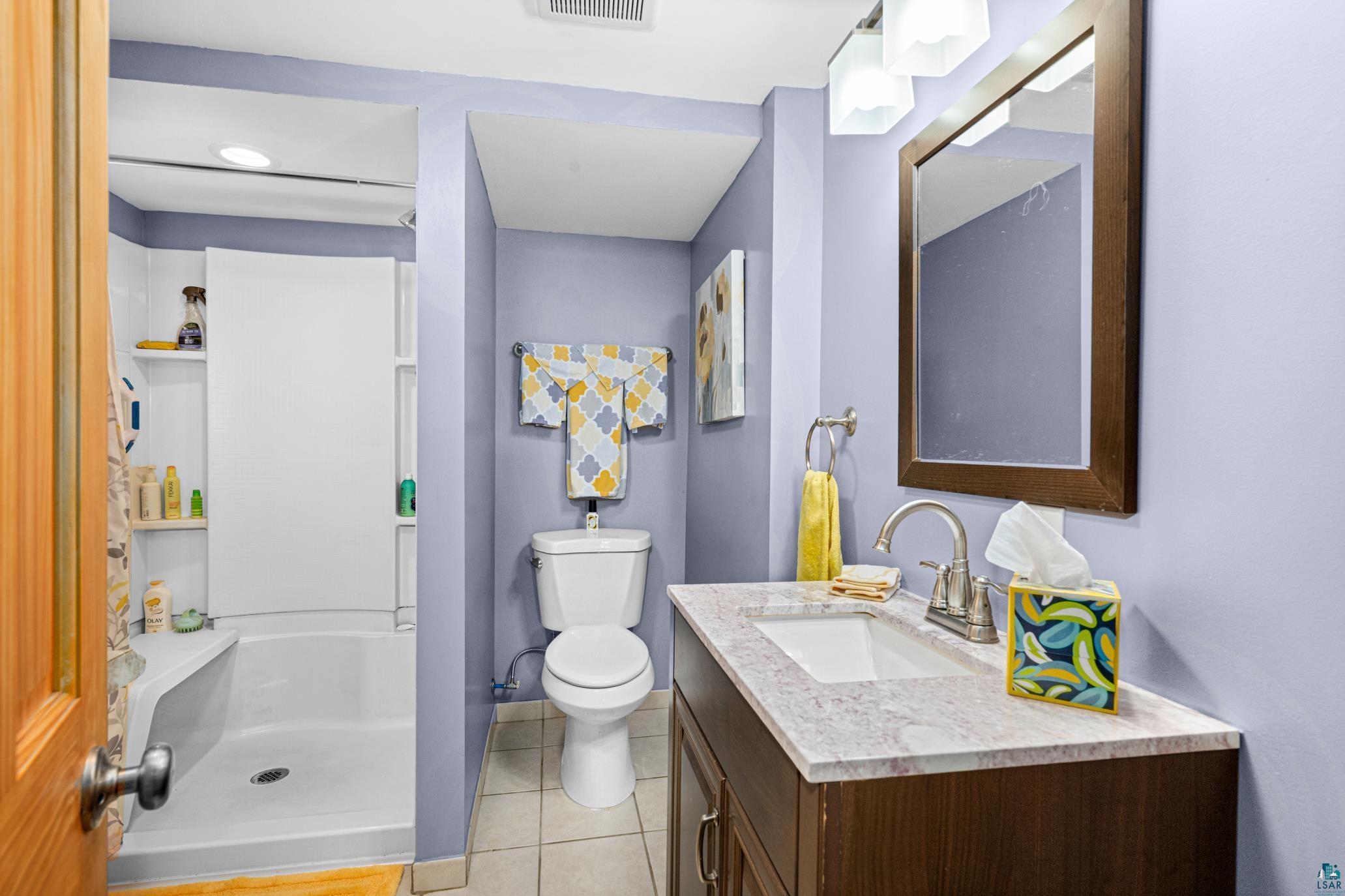 3727 Stebner Road Hermantown, MN 55811 - Photo 24 of 41 Bathroom featuring a single vanity with an integrated sink, a rectangular framed mirror, a toilet, a shower/tub combination, and tiled flooring