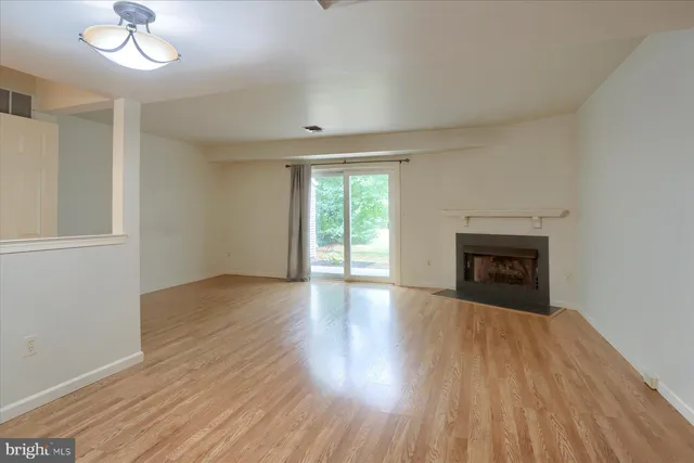 an empty room with wooden floor fireplace and windows