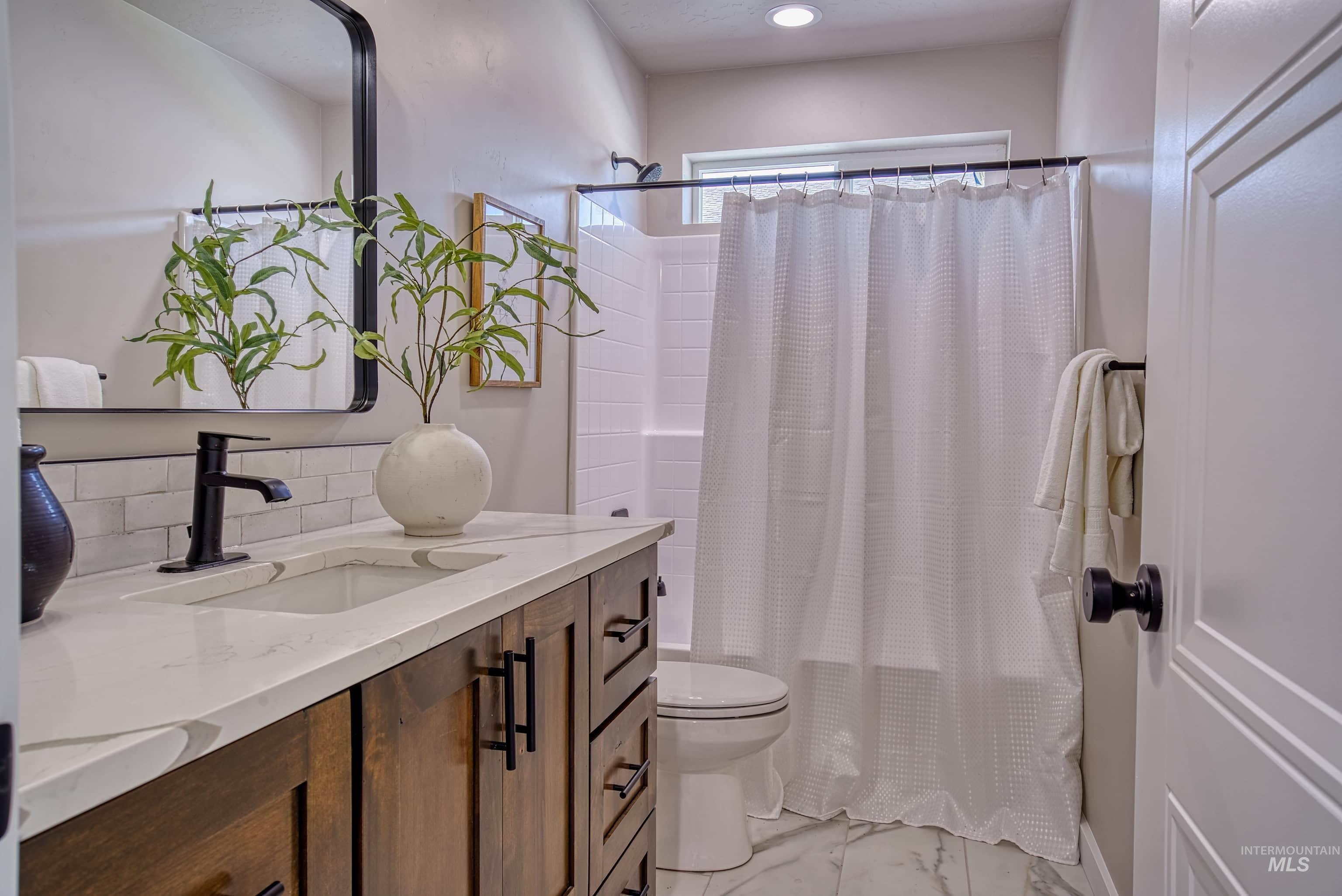 960 Campbell Street Vale, OR 97918 - Photo 11 of 49 Bathroom featuring a wood-finish vanity with a light-toned countertop, an undermount sink with a matte black faucet, a rectangular framed mirror, and a tiled shower/tub combination