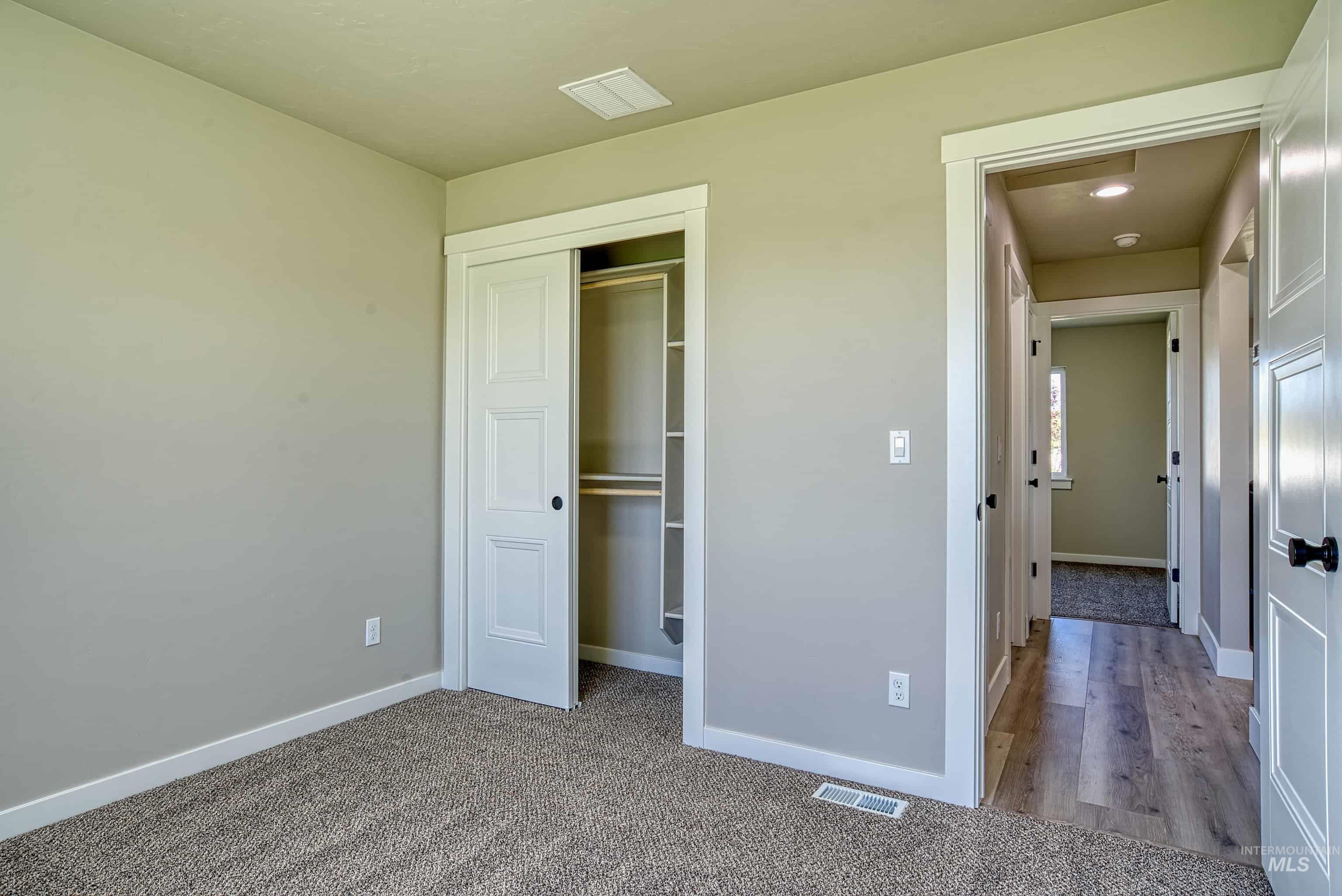 960 Campbell Street Vale, OR 97918 - Photo 31 of 49 Neutral-toned interior room featuring textured carpeting, a built-in closet with bi-fold doors, white trim, and a doorway leading to a hallway with wood-finish flooring