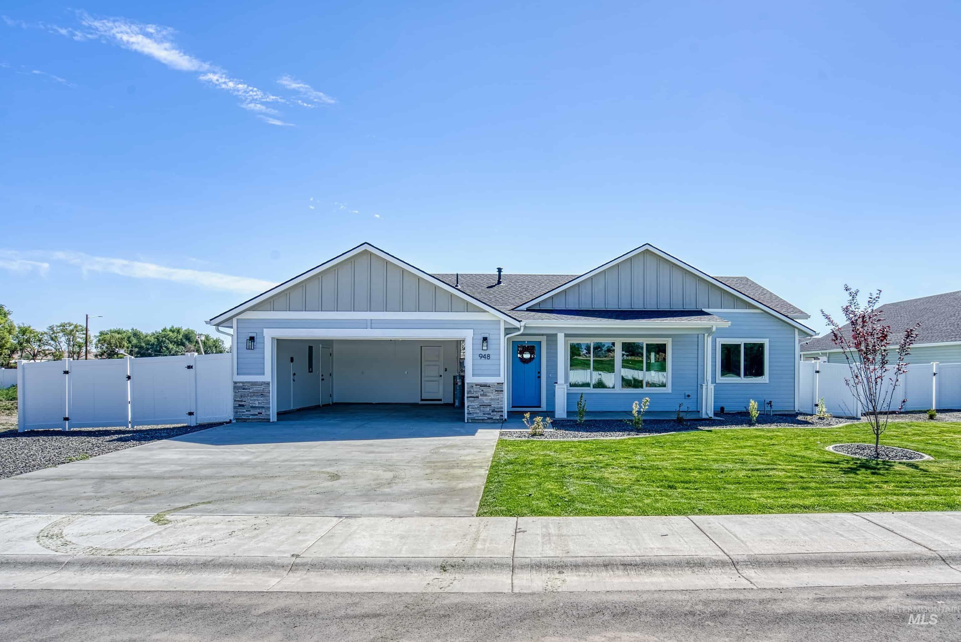 960 Campbell Street Vale, OR 97918 - Photo 45 of 49 Ranch-style exterior featuring light blue siding, a vibrant blue entry door, stone accents, a two-car garage, and a manicured lawn