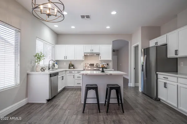 a kitchen with stainless steel appliances granite countertop a refrigerator a sink dishwasher a stove and white cabinets with wooden floor