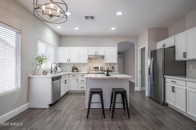 a kitchen with stainless steel appliances granite countertop a refrigerator a sink dishwasher a stove and white cabinets with wooden floor