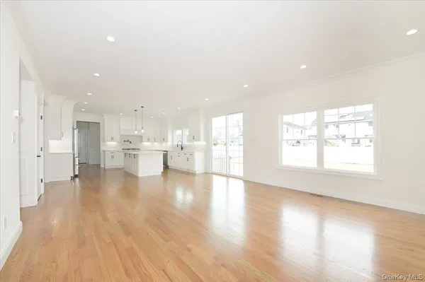 a view of an empty room with wooden floor and a kitchen