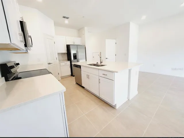 a large white room with stainless steel appliances a stove a sink a refrigerator a counter top space and cabinets