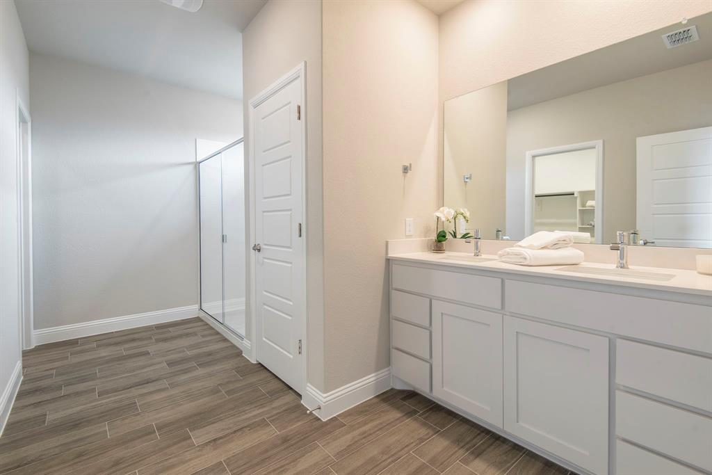 2301 Ruff Road Denton, TX 76205 - Photo 13 of 23 Modern bathroom featuring a double vanity with white cabinetry and chrome fixtures, a spacious walk-in shower with clear glass enclosure, wood-finish tile flooring, and neutral wall tones