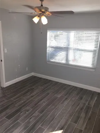 an empty room with wooden floor chandelier fan and windows