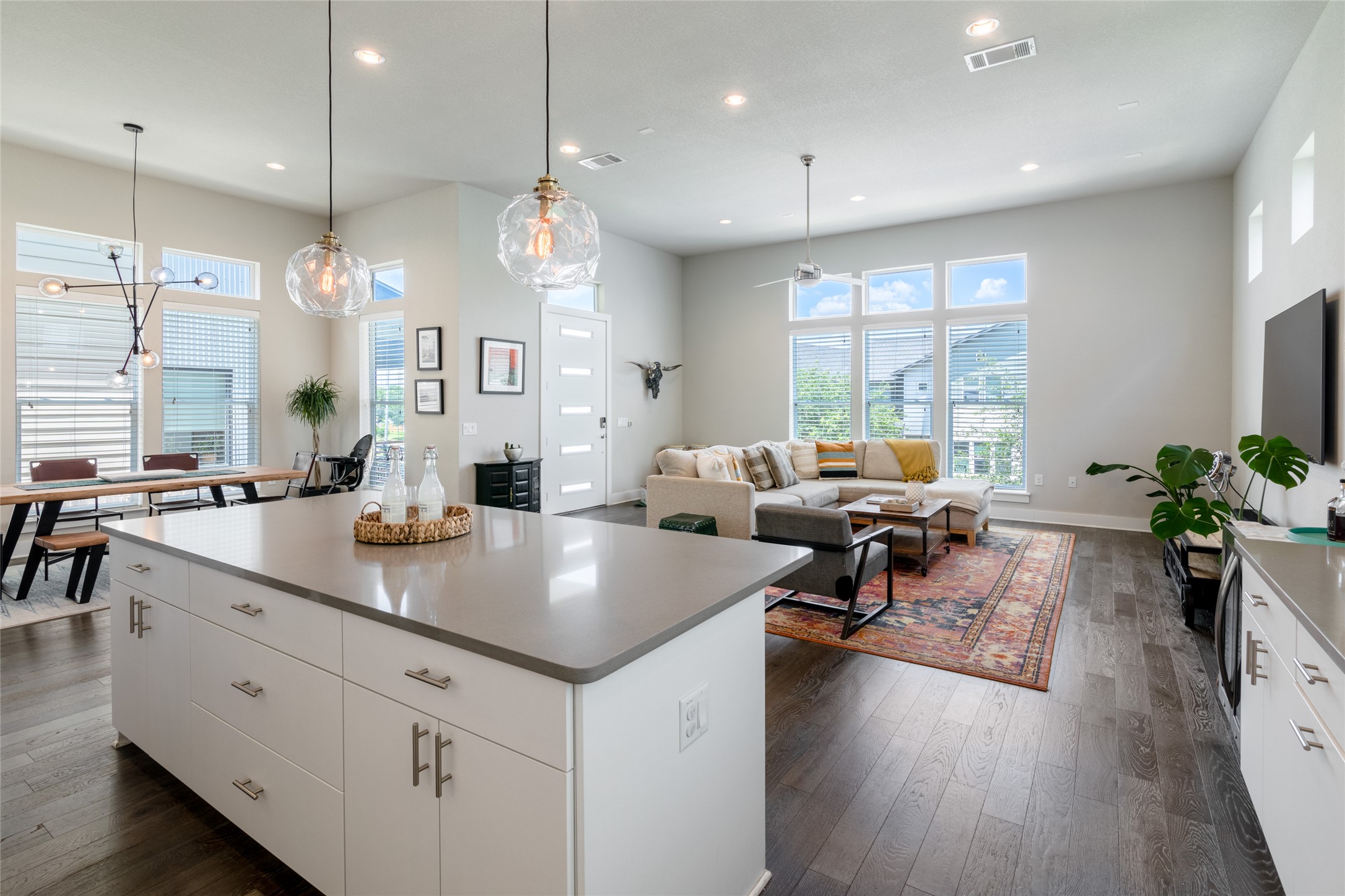 6025 Seville Drive Austin, TX 78724 - Photo 12 of 40 Large kitchen island with counter seating, a dining area with modern lighting, and a living room with expansive windows and view of open-concept living space featuring high ceilings, wood-finish flooring,