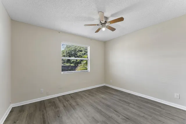 an empty room with wooden floor fan and windows