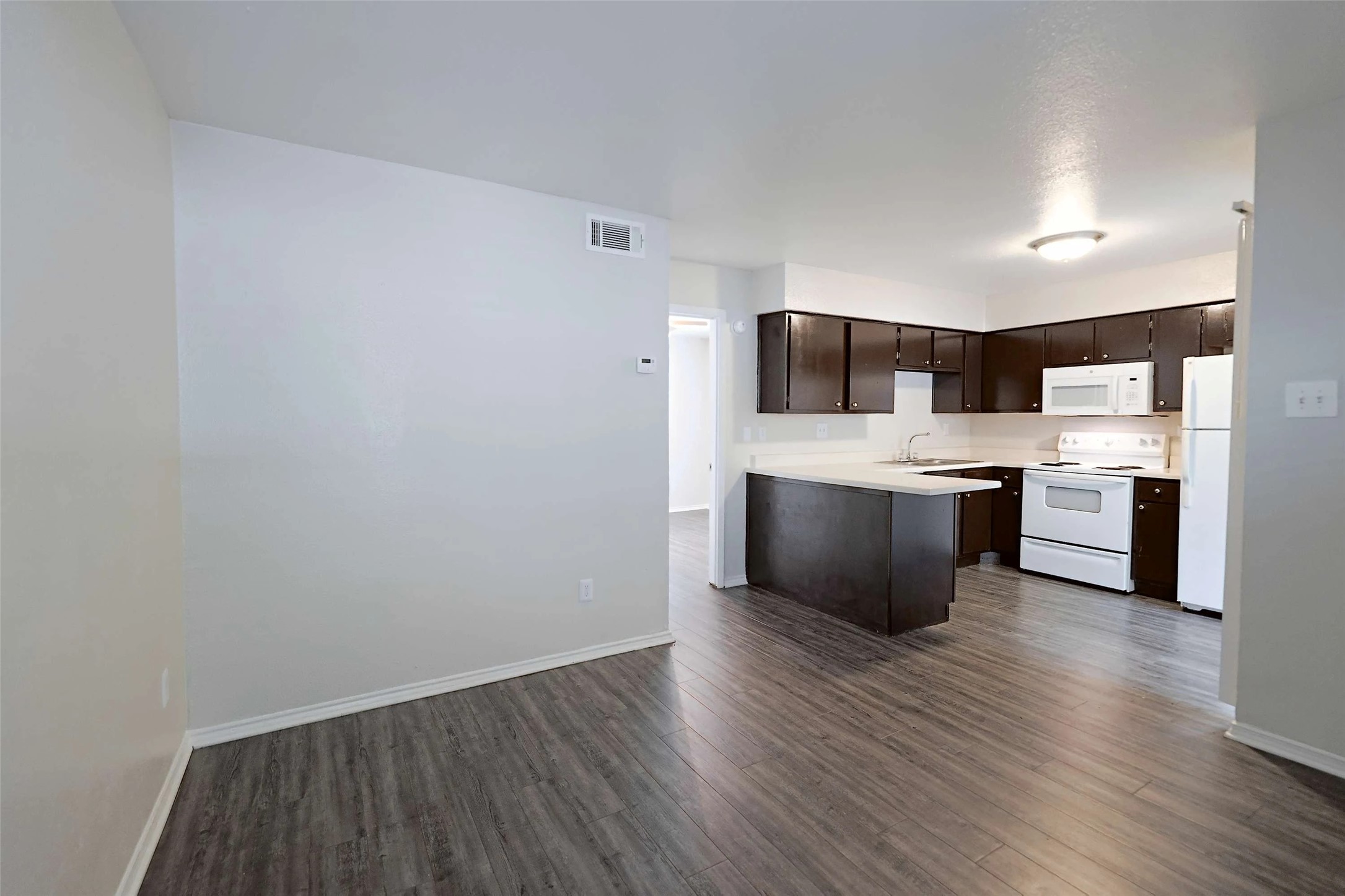 2809 West William Cannon Drive, Unit I101 Austin, TX 78745 - Photo 7 of 29 Kitchen with white appliances, light countertops, dark brown cabinets, a peninsula, and dark wood-style floors