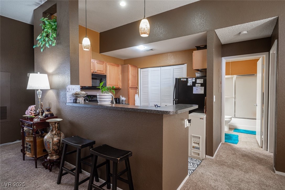 3150 North Soft Breezes Drive, Unit 2220 Las Vegas, NV 89128 - Photo 12 of 32 Kitchen with a textured wall, light carpet, light brown cabinets, decorative light fixtures, and dark countertops