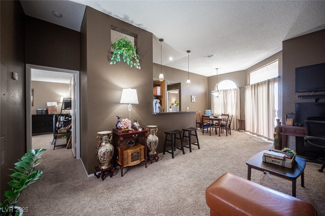 3150 North Soft Breezes Drive, Unit 2220 Las Vegas, NV 89128 - Photo 7 of 32 Living room with light carpet, a textured ceiling, a textured wall, and a chandelier