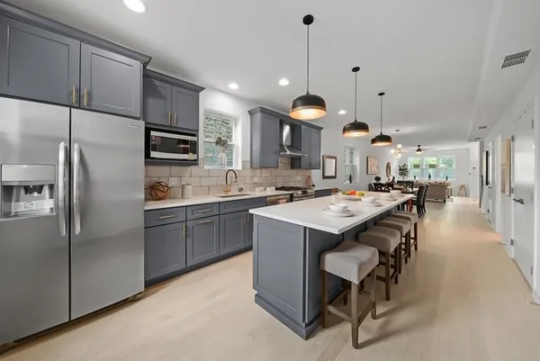 a kitchen with kitchen island a refrigerator a sink a stove and chairs with wooden floor