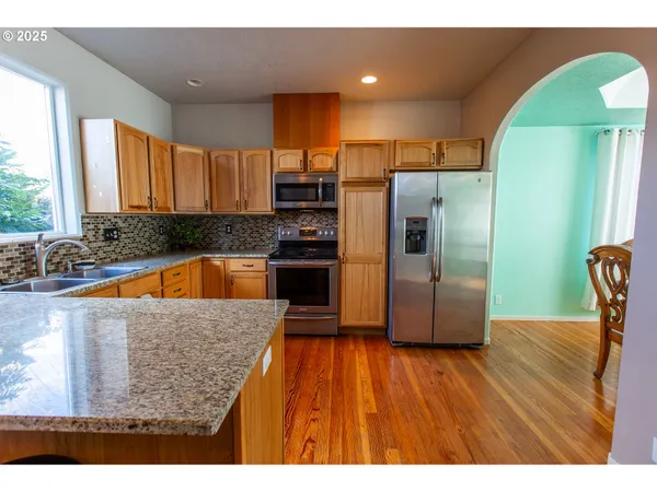 a kitchen with kitchen island granite countertop wooden floors stainless steel appliances a sink and a window