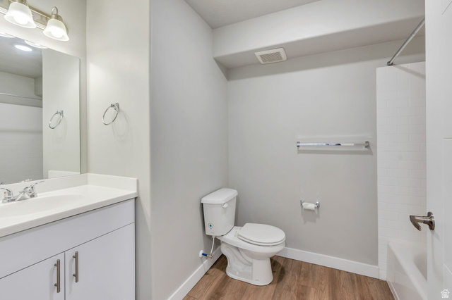 572 South 100 West, Unit E210 Springville, UT 84663 - Photo 20 of 35 Bathroom featuring a white vanity with a light-colored countertop, chrome fixtures, a toilet, a bathtub with white subway tile surround, and wood-finish flooring