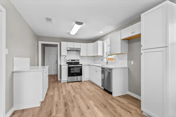 a kitchen with a refrigerator a stove top oven a white cabinets and wooden floor