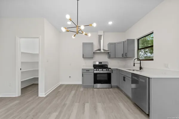 a large kitchen with stainless steel appliances a stove a sink dishwasher a refrigerator and white cabinets with wooden floor