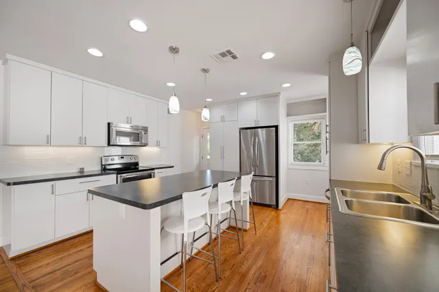 a kitchen with stainless steel appliances granite countertop a refrigerator a sink a stove and white cabinets with wooden floor