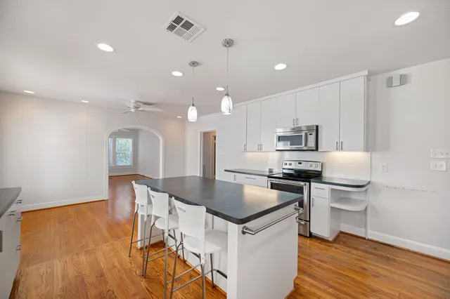 a kitchen with stainless steel appliances a stove a sink a kitchen island with chairs and wooden floor