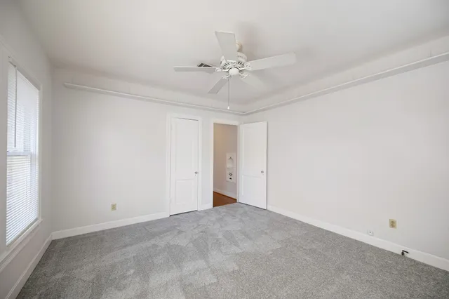 an empty room with chandelier fan and windows