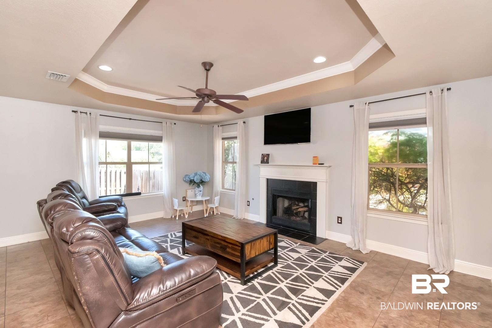 27890 Rileywood Drive Daphne, AL 36526 - Photo 19 of 49 Tiled living room featuring ceiling fan, a tiled fireplace, baseboards, visible vents, and a raised ceiling