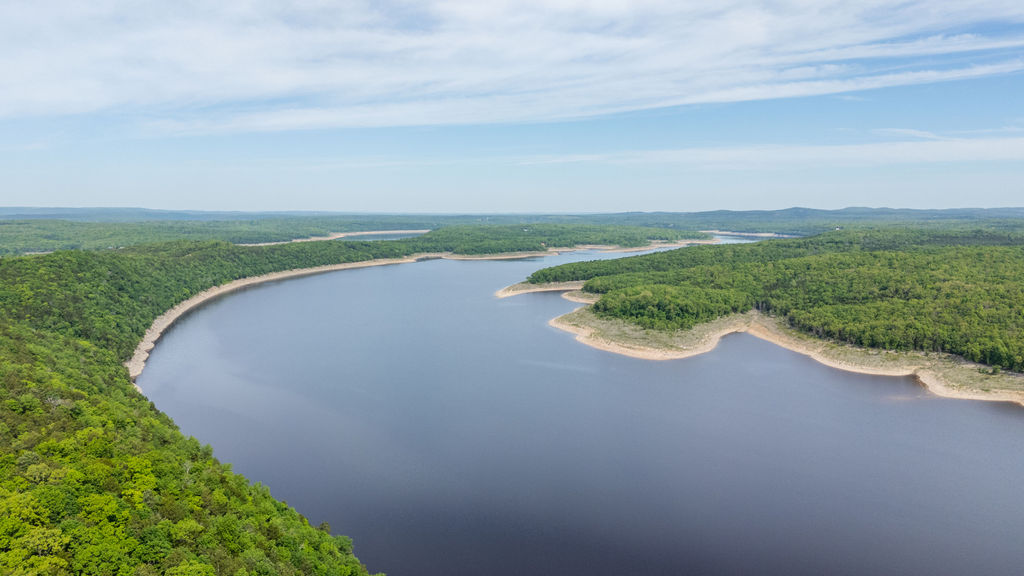 Expansive body of water bordered by dense green forests and a clear sky