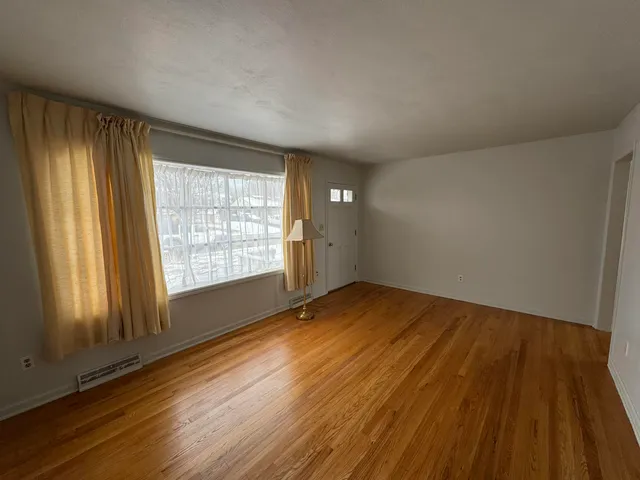 a view of an empty room with wooden floor and a window