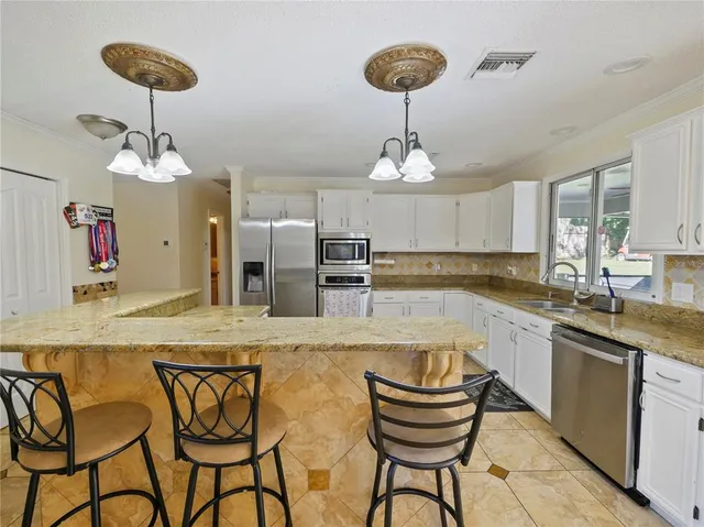 a kitchen with stainless steel appliances kitchen island granite countertop a refrigerator a stove a sink dishwasher and white cabinets with wooden floor