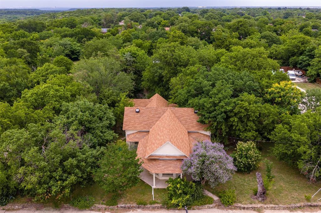 1007 West Belt Line Road Cedar Hill, TX 75104 - Photo 17 of 30 Residential structure featuring a brown shingle roof, light-colored siding, and a covered front porch, surrounded by extensive mature trees and established landscaping