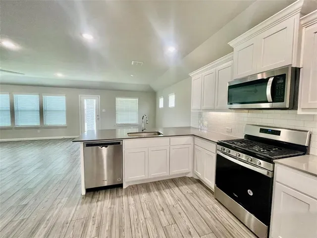 a kitchen with granite countertop a stove top oven a sink dishwasher and white cabinets with wooden floor
