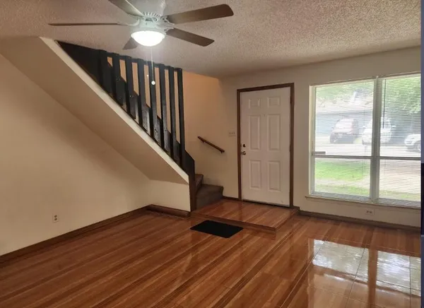 a view of an empty room with wooden floor and fan