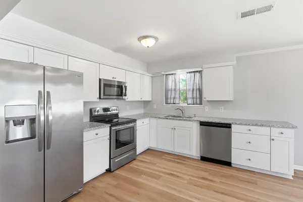 a kitchen with stainless steel appliances granite countertop a stove top oven a sink and dishwasher a refrigerator with wooden floor