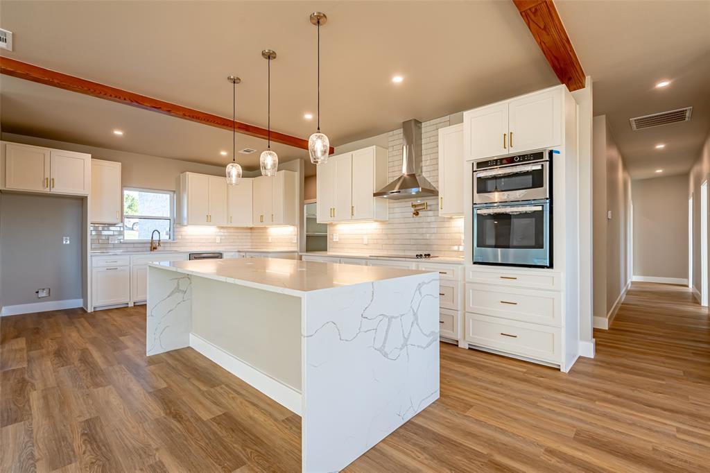 2128 Eagles Rdg Drive Weatherford, TX 76087 - Photo 29 of 39 Kitchen featuring beamed ceiling, a kitchen island, white cabinets, decorative backsplash, and light stone countertops