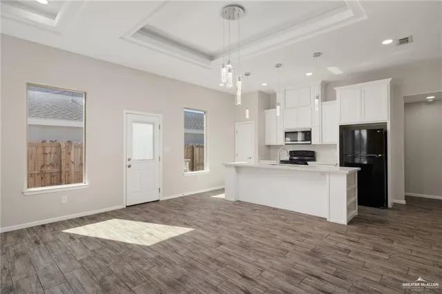 a kitchen with stainless steel appliances kitchen island granite countertop a refrigerator oven a sink dishwasher and white cabinets with wooden floor