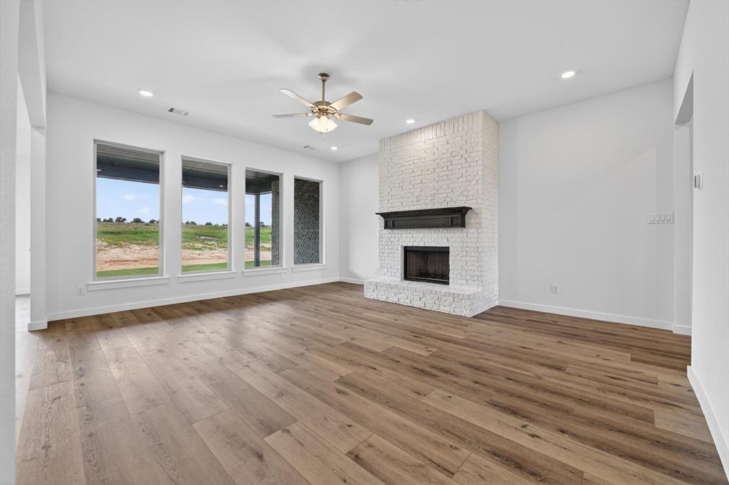 416 McAlpine Drive Springtown, TX 76082 - Photo 8 of 40 Spacious living area featuring expansive wood-finish flooring, a white-painted brick fireplace with a dark mantel, multiple large windows, recessed lighting, and a ceiling fan