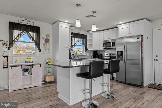 a kitchen with stainless steel appliances kitchen island granite countertop a refrigerator a stove top oven a sink dishwasher and white cabinets with wooden floor