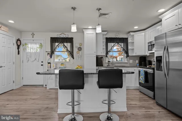 a kitchen with stainless steel appliances granite countertop a refrigerator a stove a microwave oven a sink dishwasher and white cabinets with wooden floor