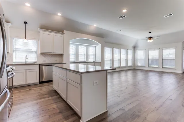 a kitchen with stainless steel appliances granite countertop a stove a sink dishwasher a refrigerator and white cabinets with wooden floor