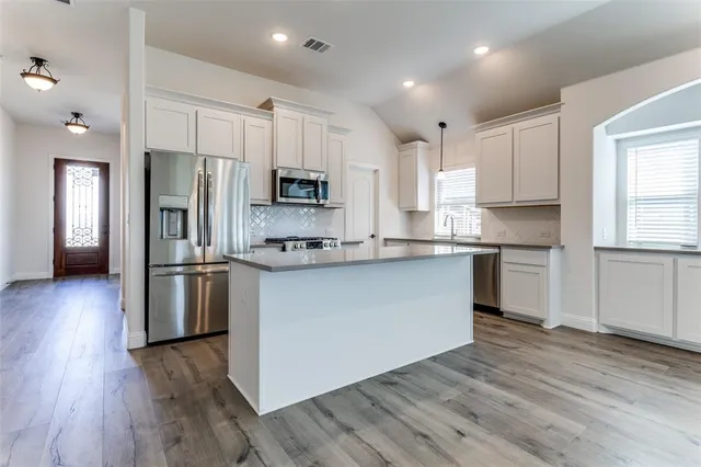 a kitchen with stainless steel appliances granite countertop a refrigerator a stove top oven a sink and dishwasher with wooden floor