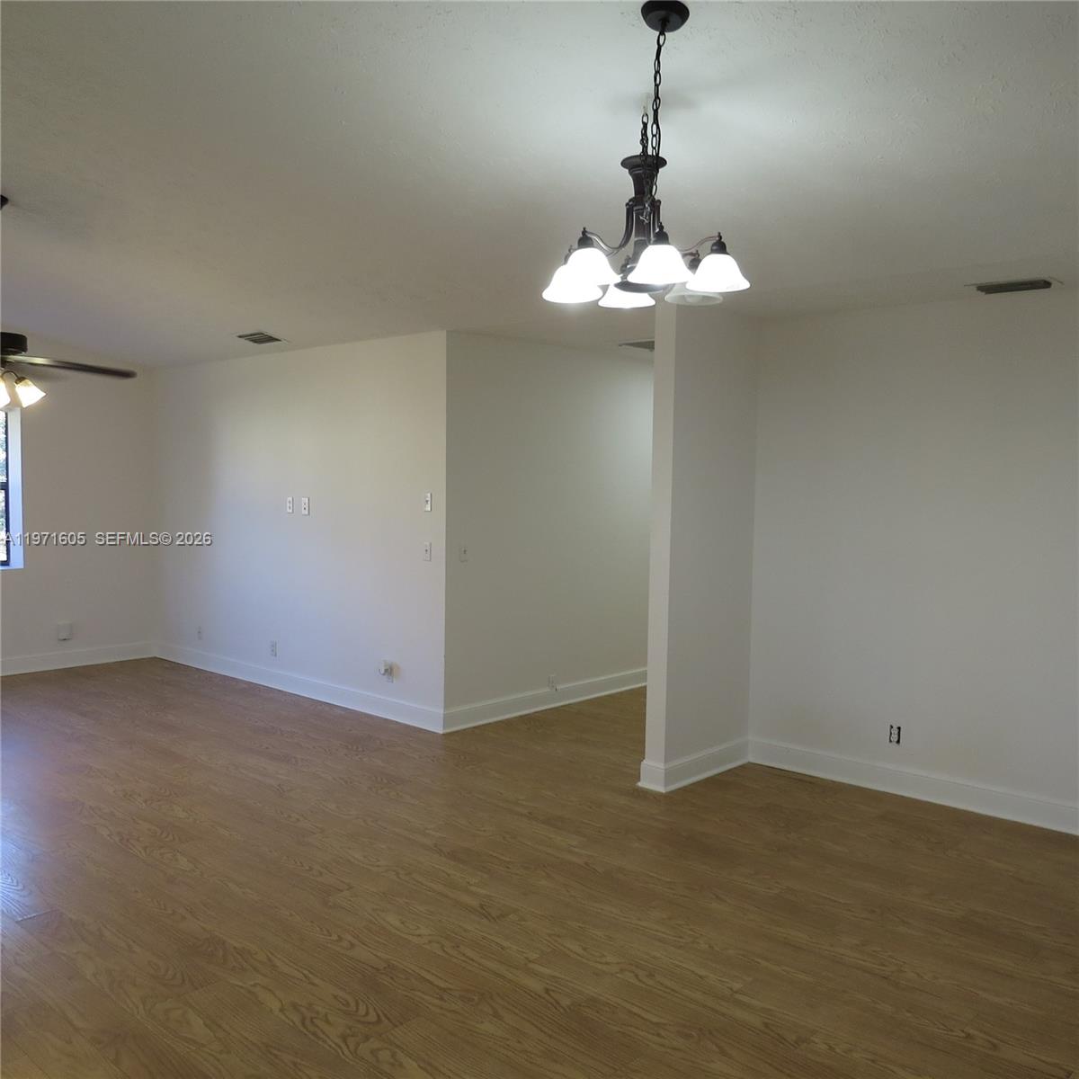 6883 Southeast Raintree Avenue Stuart, FL 34997 - Photo 5 of 32 an empty room with a chandelier fan and wooden floor